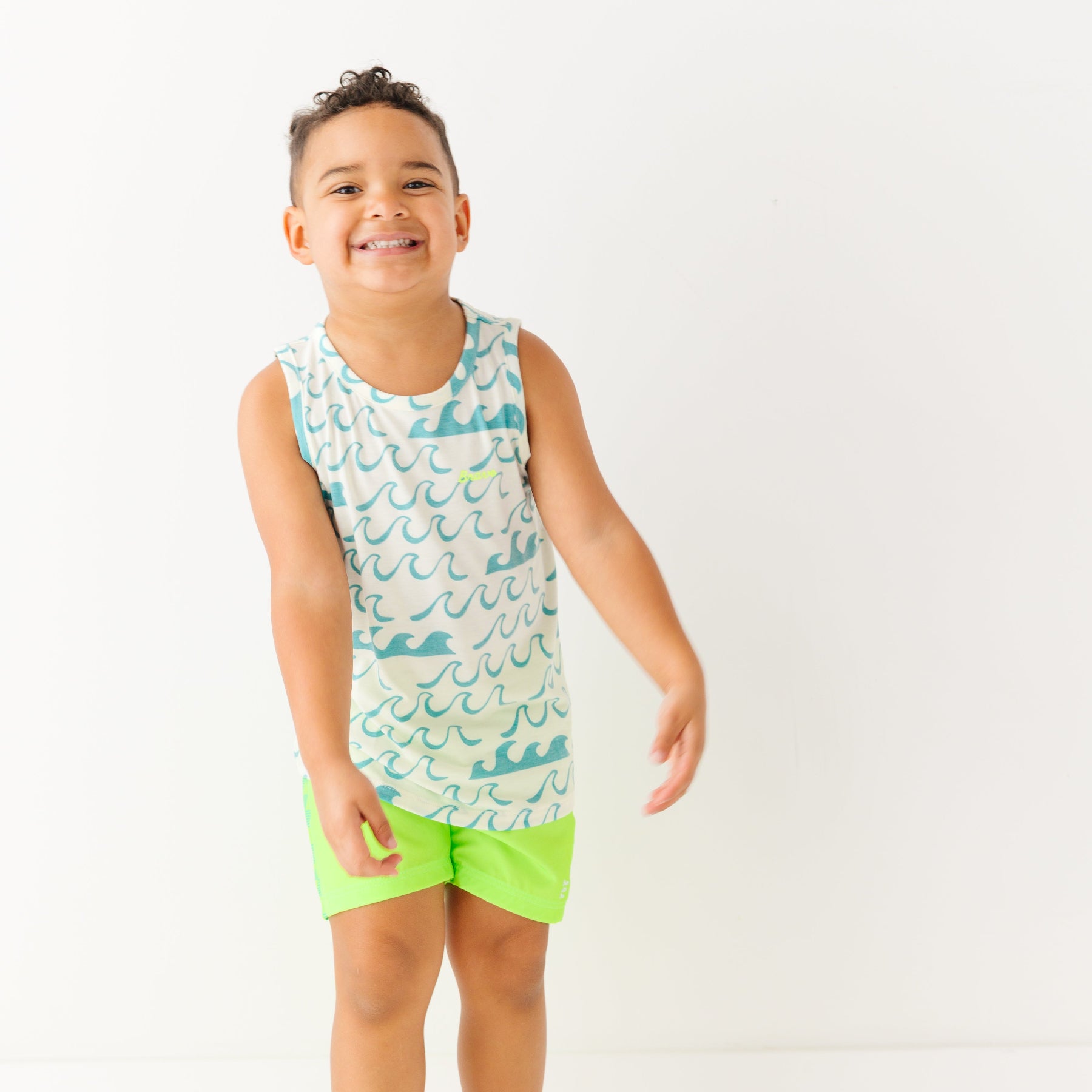 Child wearing a green checkered swim trunks and a wave-patterned top on a white background