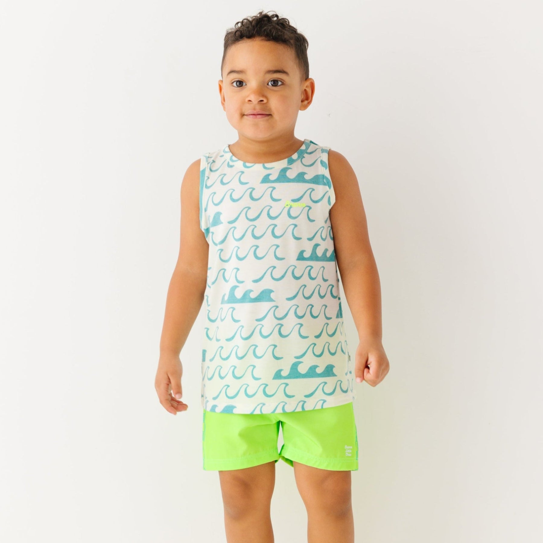 Child wearing a green checkered swim trunks and a wave-patterned top on a white background
