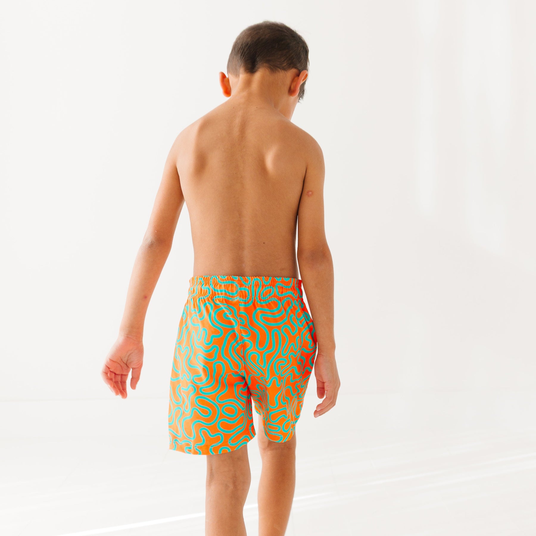 Child wearing orange and blue squiggly-patterned swim shorts on a white background