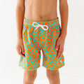 Close up of a child wearing orange and blue squiggly-patterned swim shorts on a white background