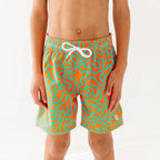 Close up of a child wearing orange and blue squiggly-patterned swim shorts on a white background