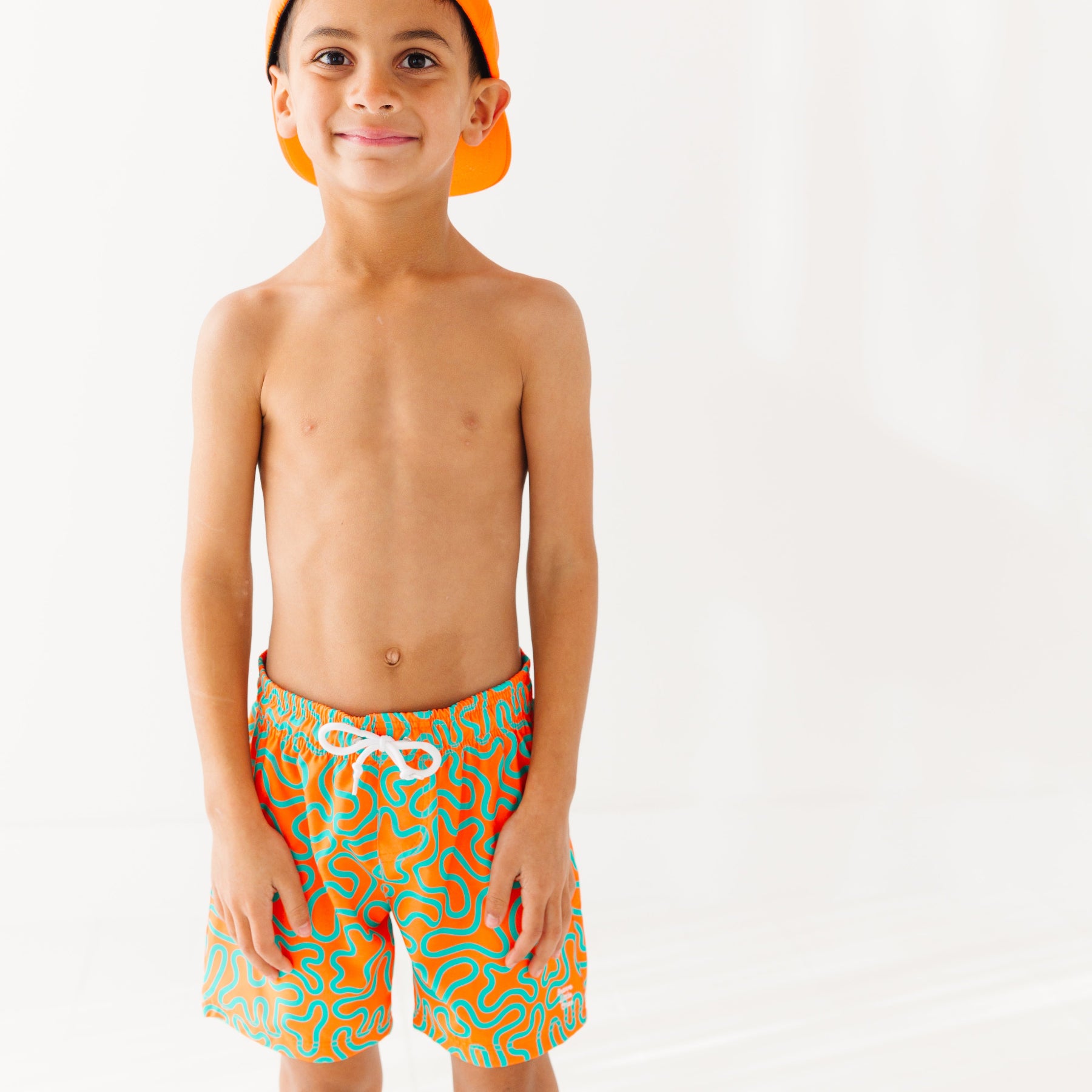 Child wearing orange and blue squiggly-patterned swim shorts on a white background