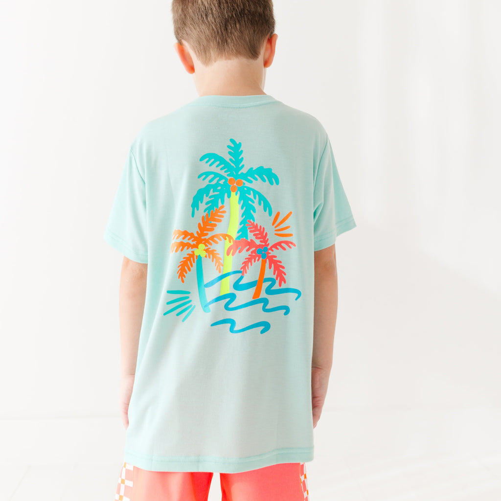 Back view of a child wearing a light blue t-shirt with colorful palm tree design on a white background