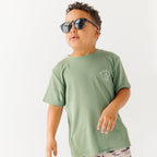 Child wearing a green t-shirt with a graphic, camouflage shorts and sunglasses on a white background
