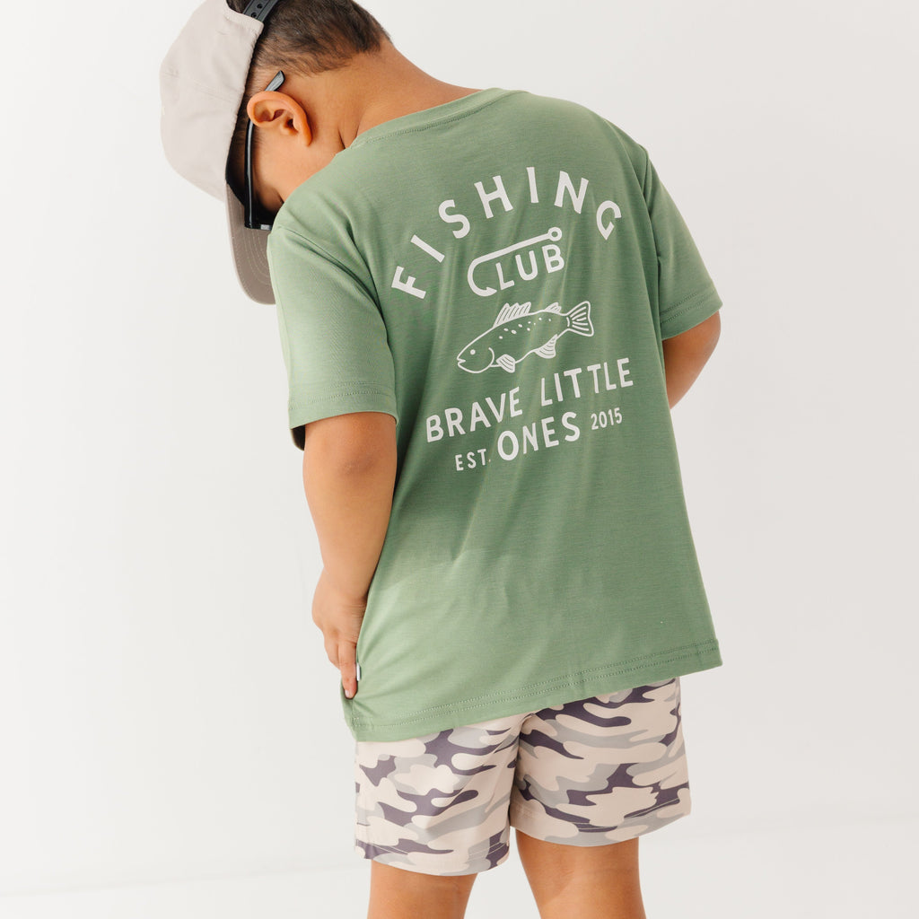 Child wearing a green t-shirt with 'Fishing Club' text and camouflage shorts on a white background