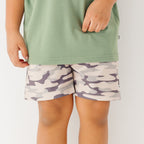 Close up of a child wearing a green shirt and camouflage shorts on a white background