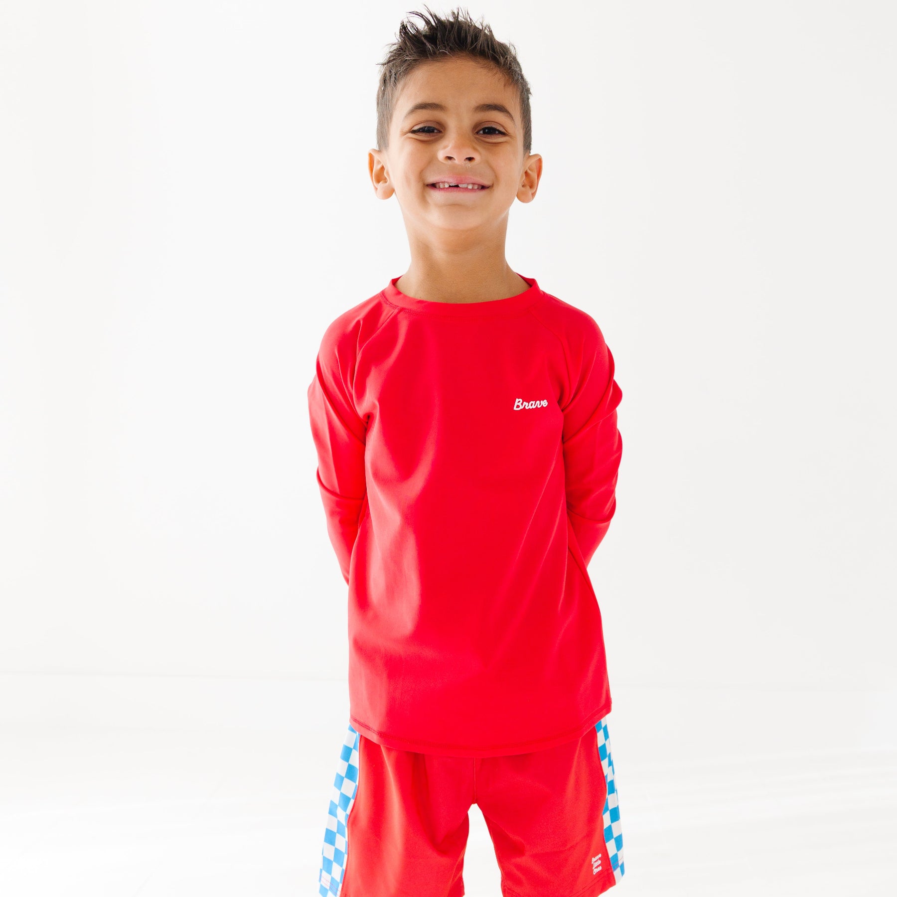 Child wearing a red rash guard and matching red swim trunks on a white background