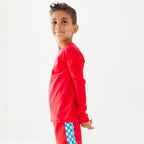 Child wearing a red rash guard and matching red swim trunks on a white background