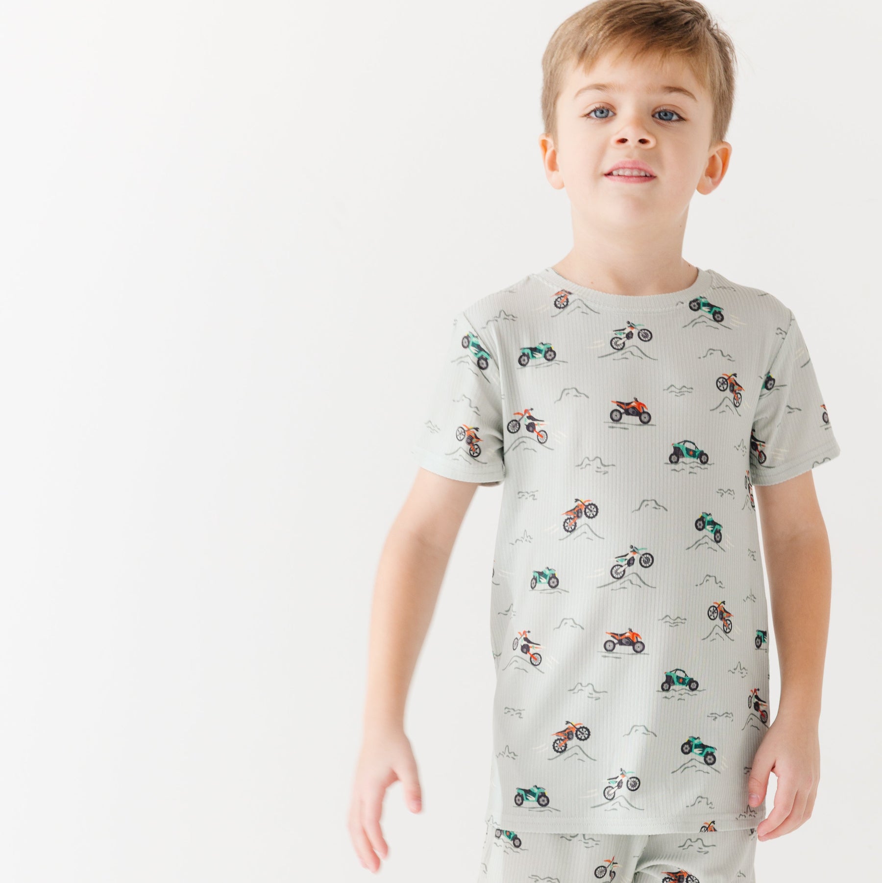 Child wearing a light gray short pajama set with vehicle pattern on a white background