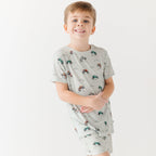 Child wearing a light gray short pajama set with vehicle pattern on a white background