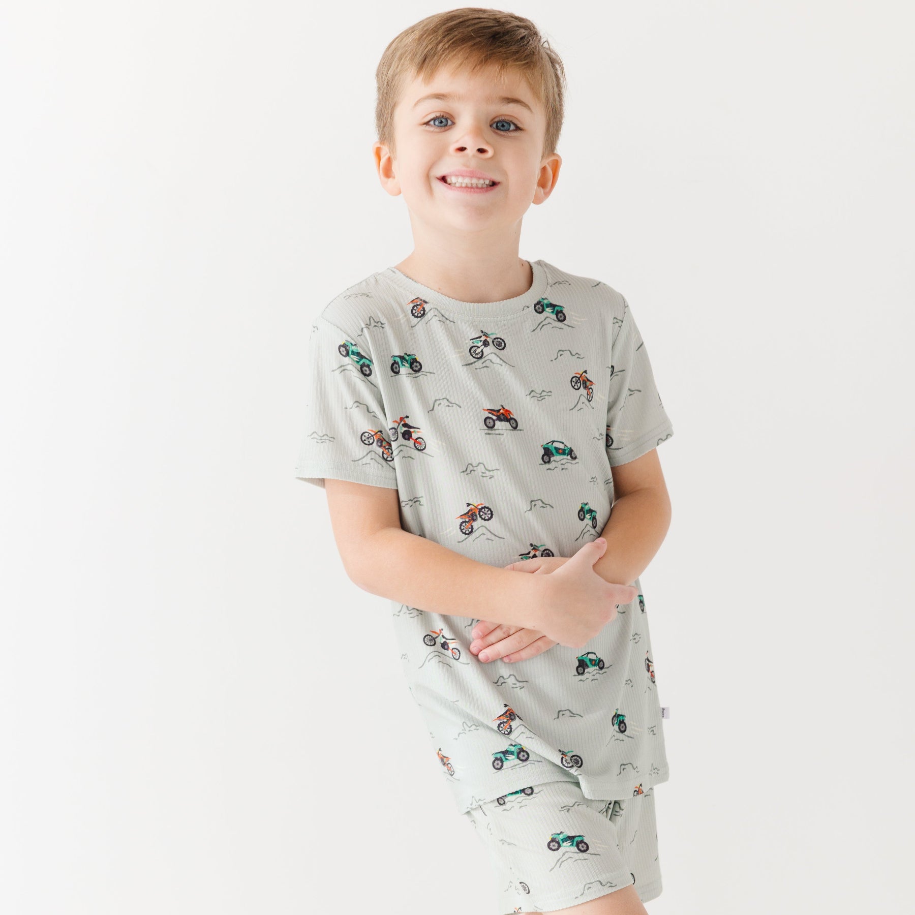 Child wearing a light gray short pajama set with vehicle pattern on a white background