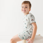 Child wearing a light gray short pajama set with vehicle pattern on a white background