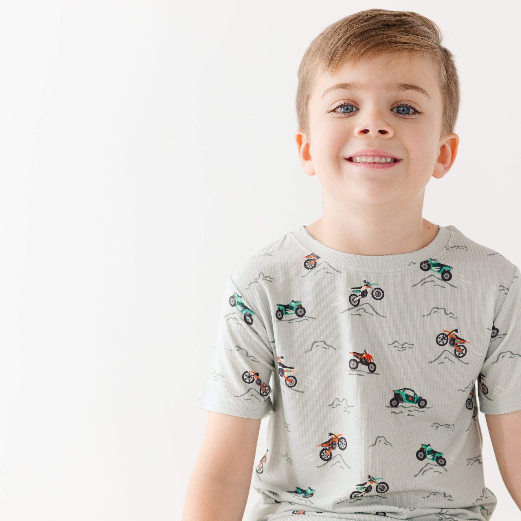 Child wearing a light gray short pajama set with vehicle pattern on a white background