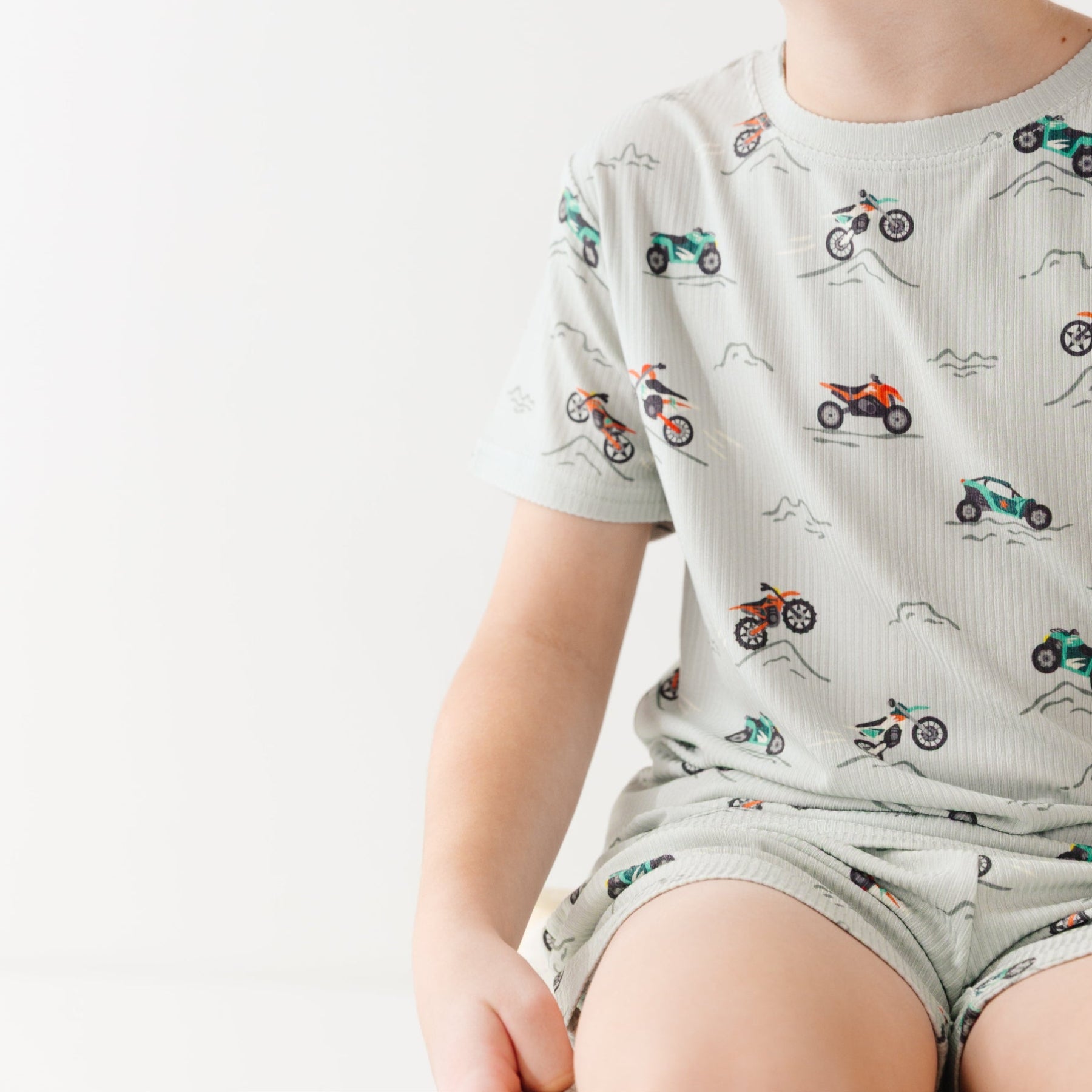 Child wearing a light gray short pajama set with vehicle pattern on a white background