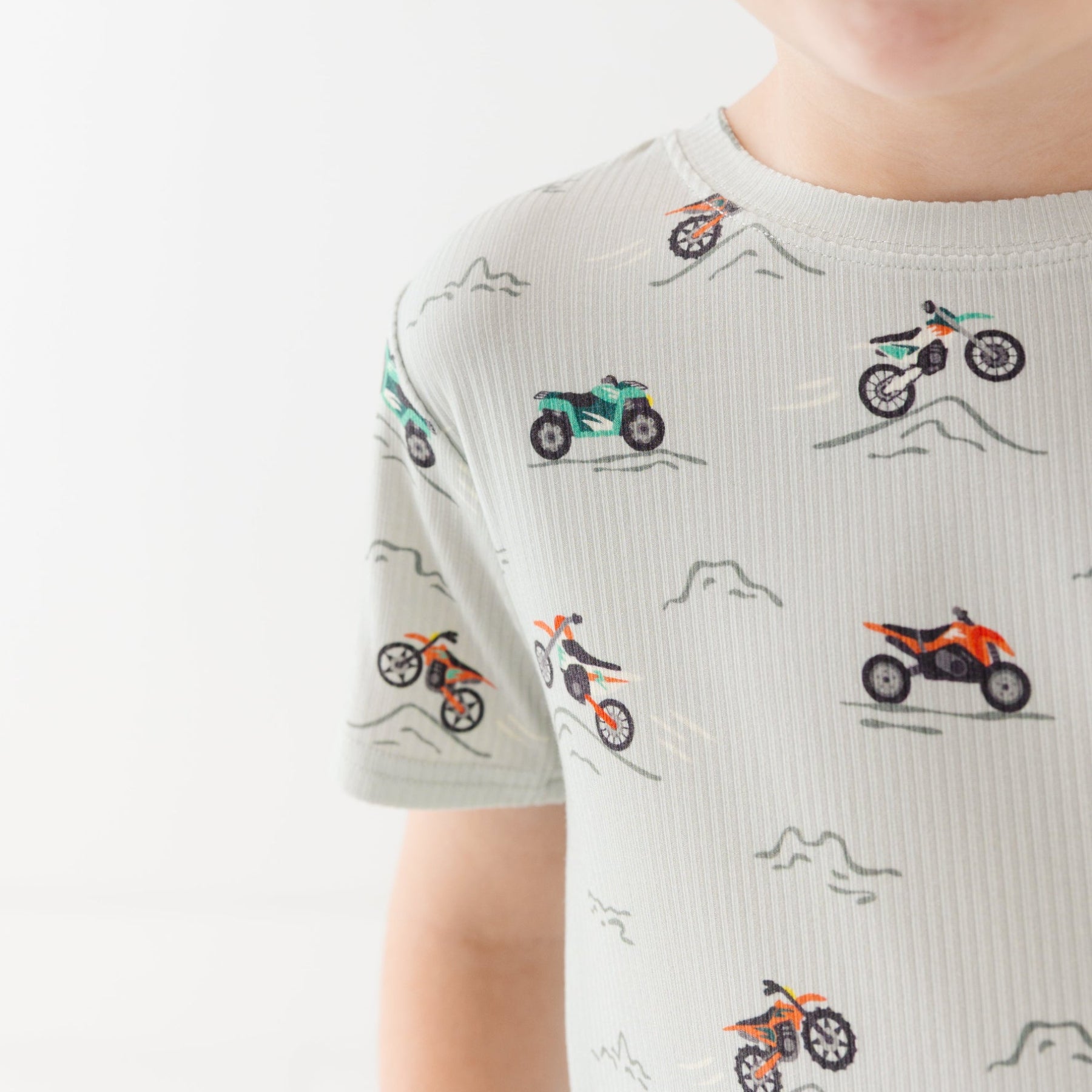 Close up shot of a child wearing a light gray shirt with vehicle pattern on a white background