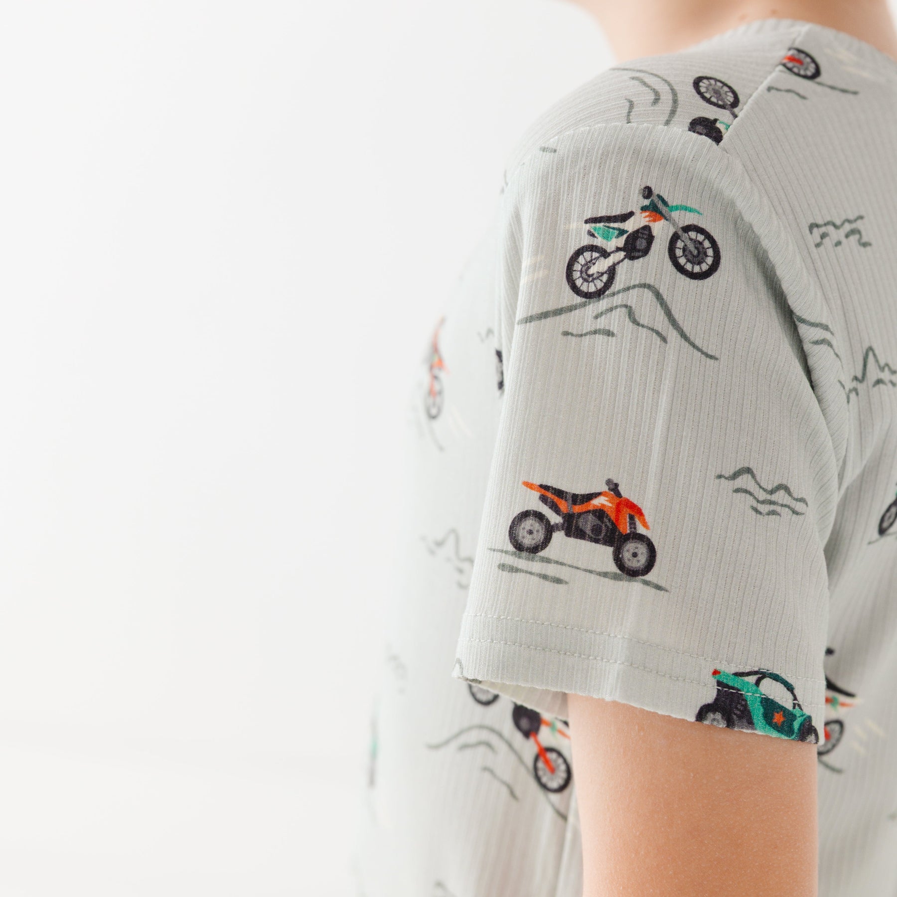 Close up shot of a child wearing a light gray shirt with vehicle pattern on a white background