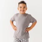 Child wearing a gray t-shirt and geometric-patterned shorts on a white background