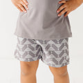 Close up shot of a child wearing a gray t-shirt and geometric-patterned shorts on a white background