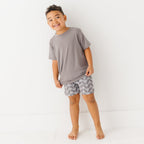 Child wearing a gray t-shirt and geometric-patterned shorts on a white background