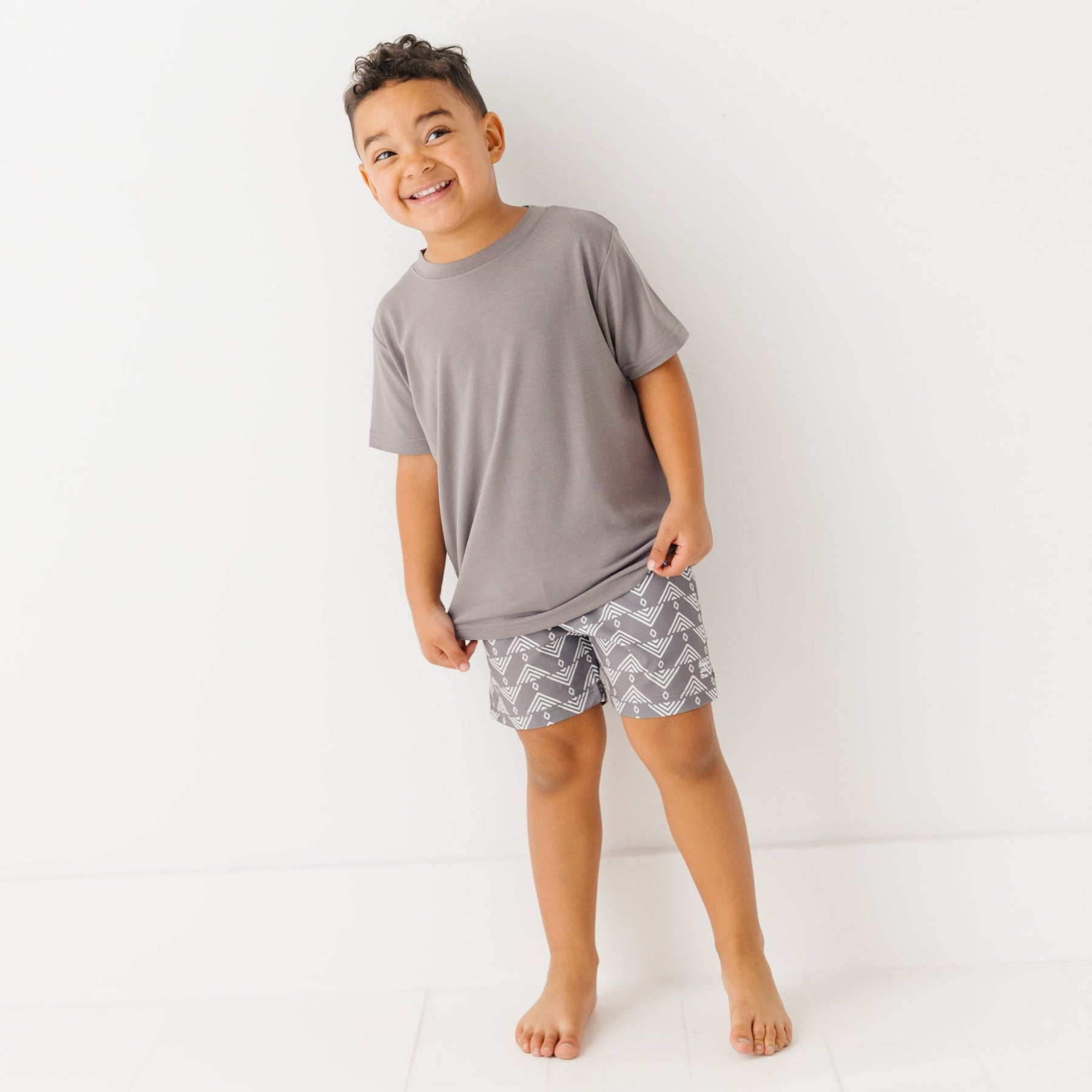 Child wearing a gray t-shirt and geometric-patterned shorts on a white background