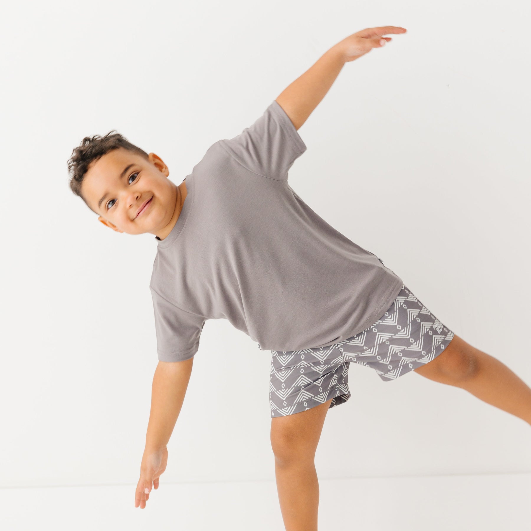 Child wearing a gray t-shirt and geometric-patterned shorts on a white background
