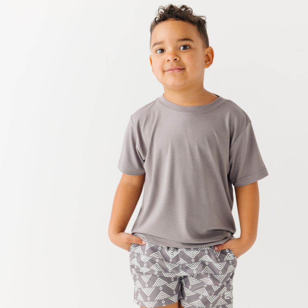 Child wearing a gray t-shirt and geometric-patterned shorts on a white background