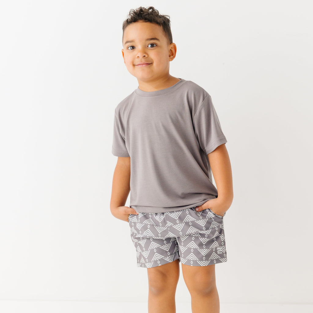 Child wearing a gray t-shirt and geometric-patterned shorts on a white background