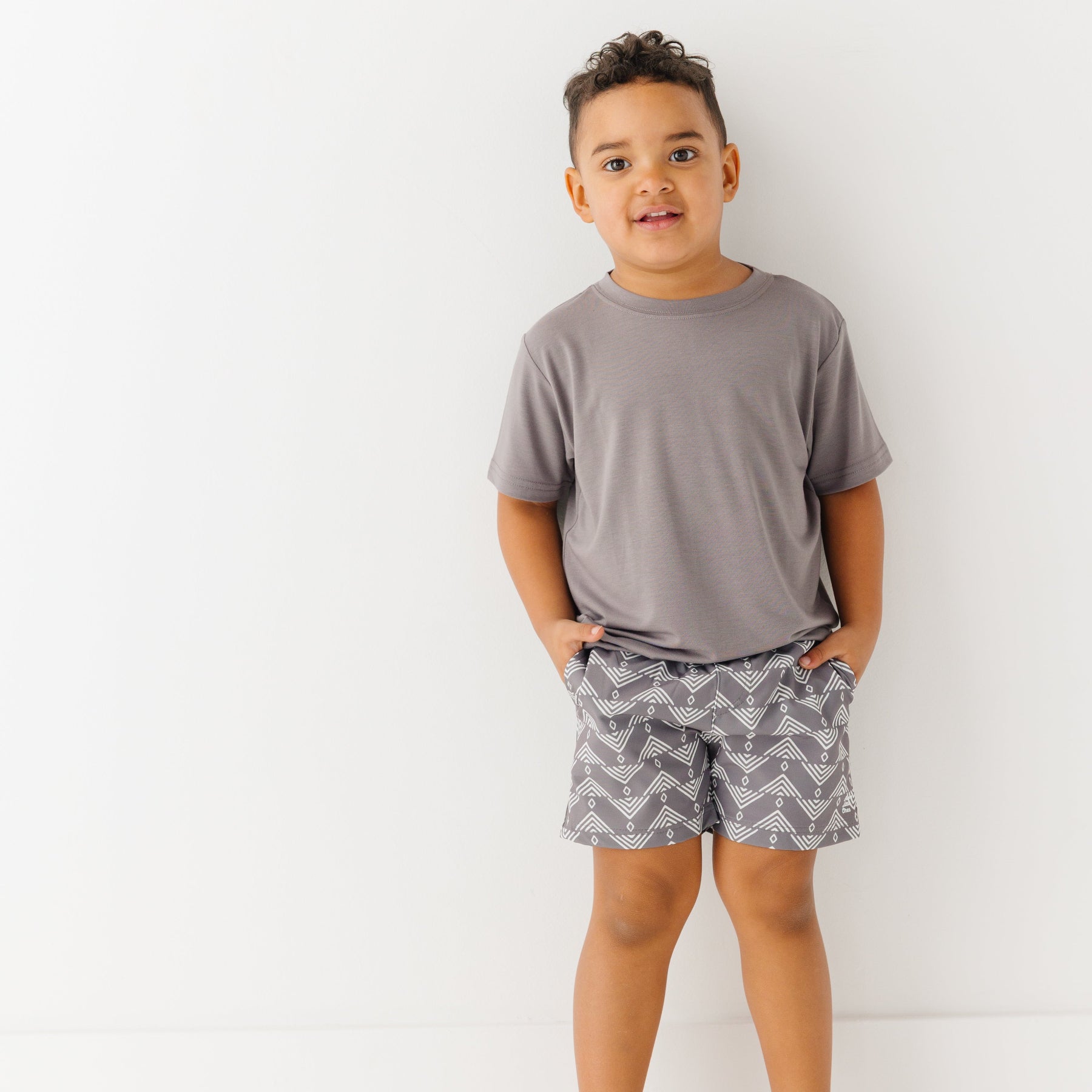 Child wearing a gray t-shirt and geometric-patterned shorts on a white background