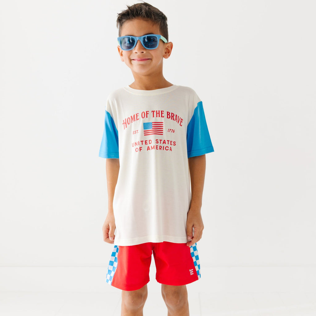 Child wearing a white t-shirt with blue sleeves and red shorts, wearing sunglasses on a white background
