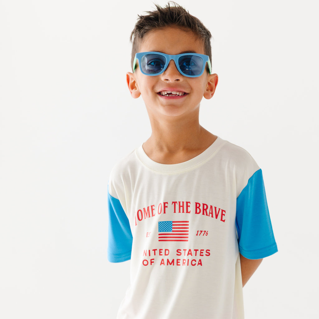 Child wearing a white t-shirt with blue sleeves and blue sunglasses on a white background