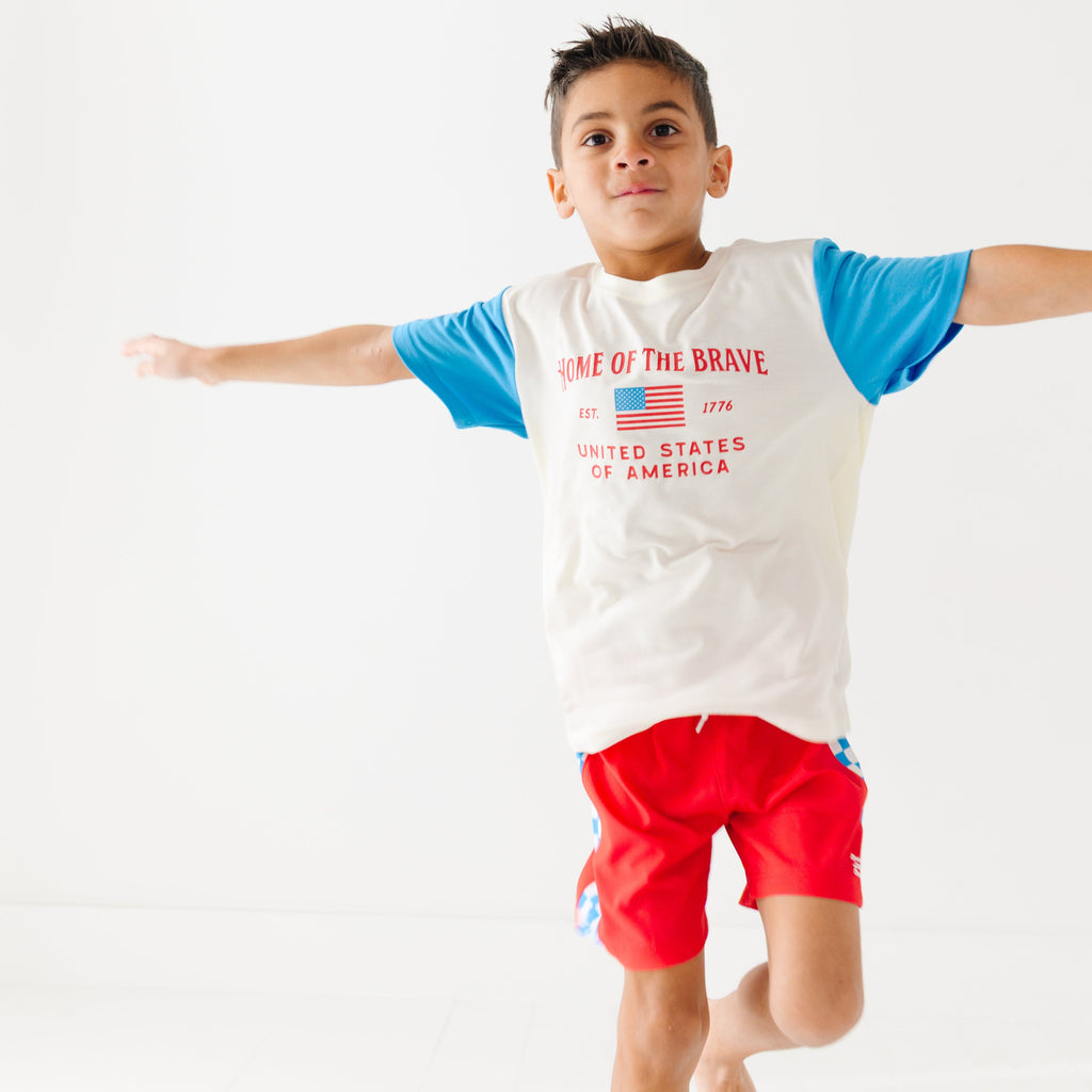 Child wearing a white t-shirt with blue sleeves and red shorts on a white background
