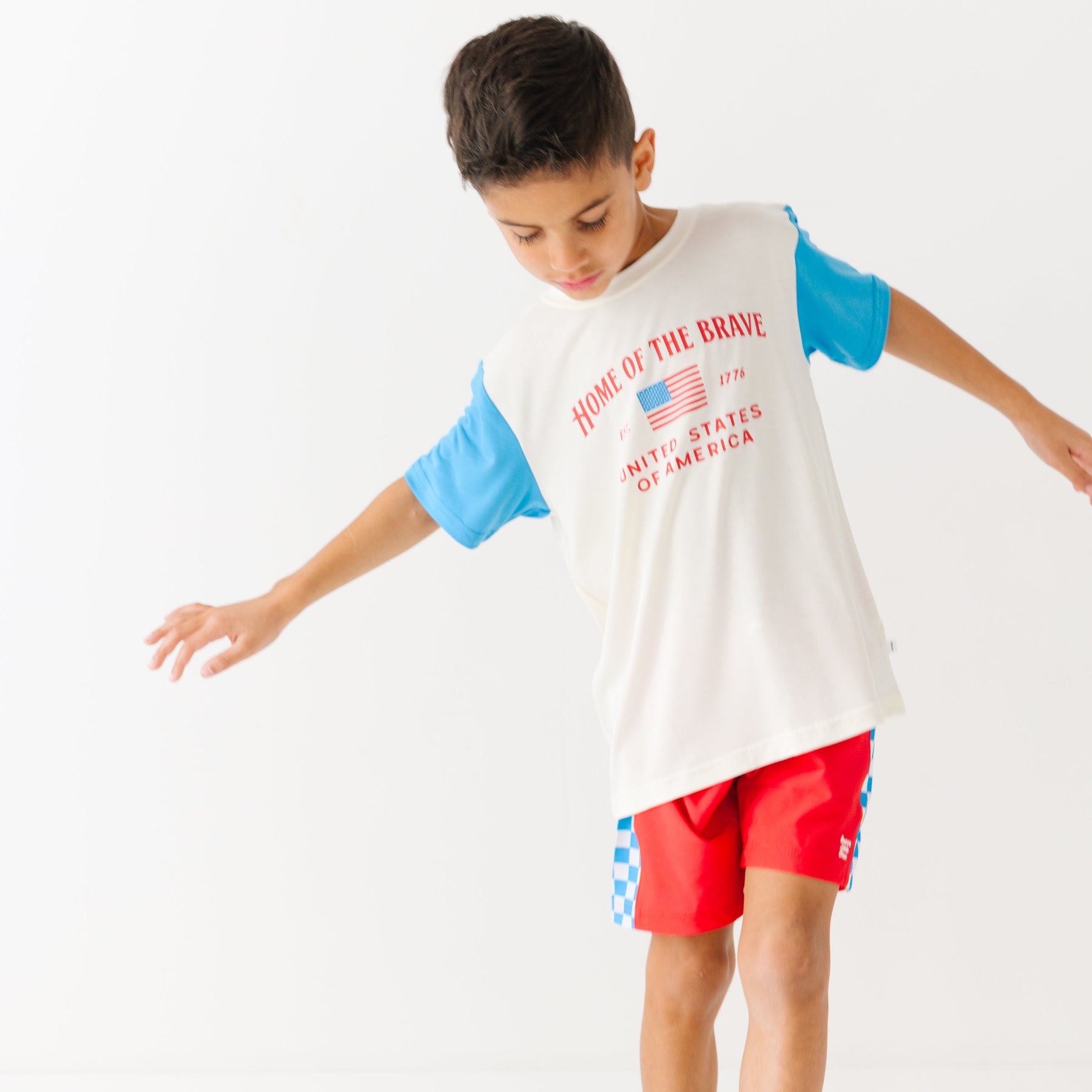 Child wearing a white t-shirt with blue sleeves and red shorts on a white background