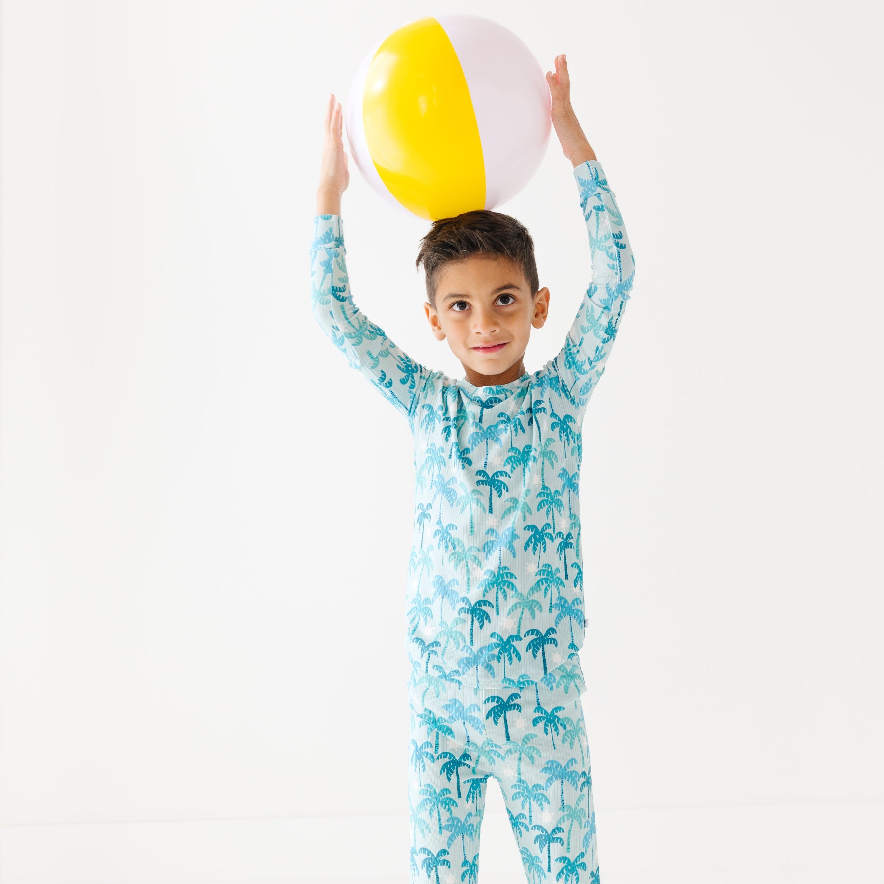 Child wearing a palm tree patterned pajama set holding a beach ball.
