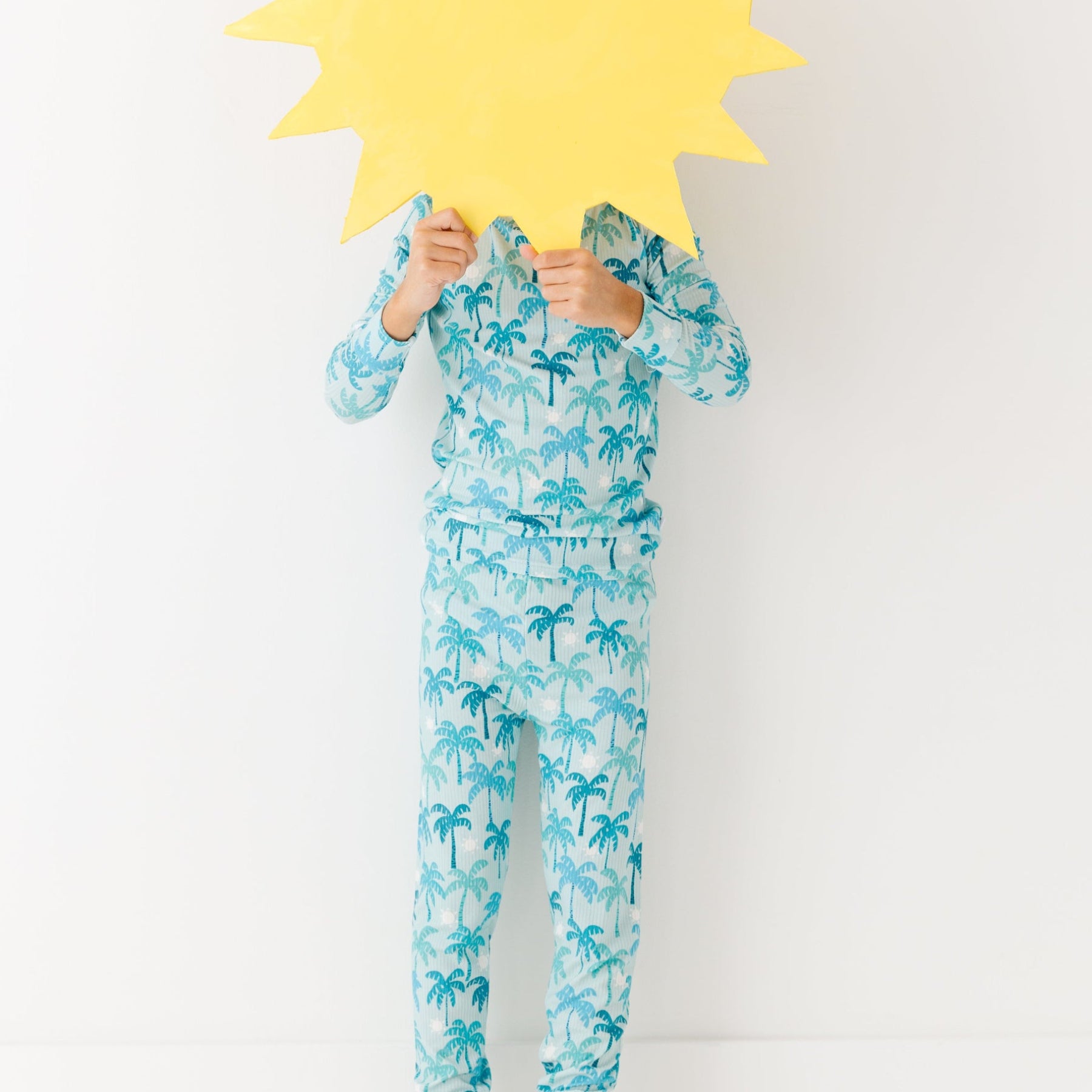 Child wearing a blue palm tree patterned pajama set holding a yellow sun-shaped object.