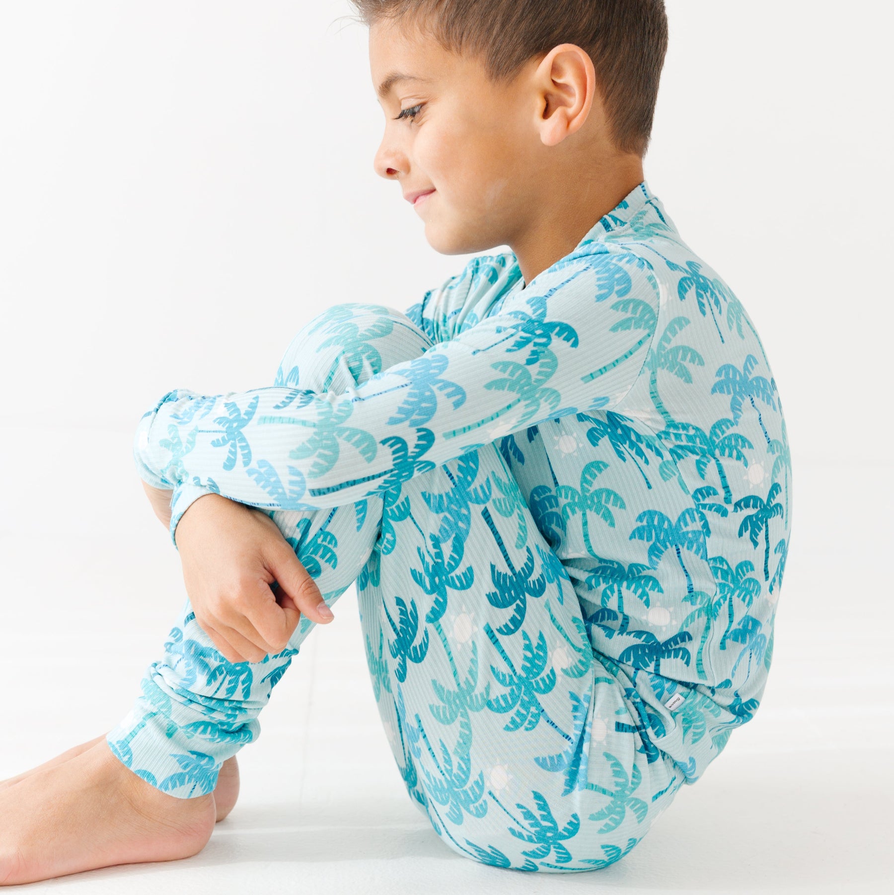 Child wearing a blue palm tree patterned pajama set on a white background.