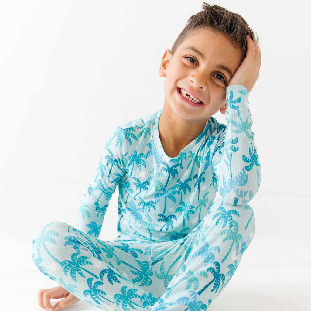 Child wearing a blue palm tree patterned pajama set on a white background.