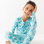 Child wearing a blue palm tree patterned pajama set on a white background.