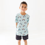 Child wearing a light blue t-shirt with vehicle pattern and black shorts on a white background