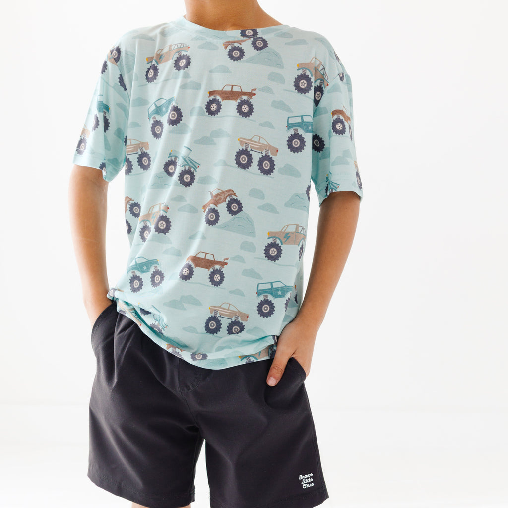Child wearing a light blue t-shirt with vehicle patterns and black shorts on a white background