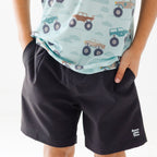 Close up shot of a child wearing a light blue shirt with vehicle prints and black shorts on a white background