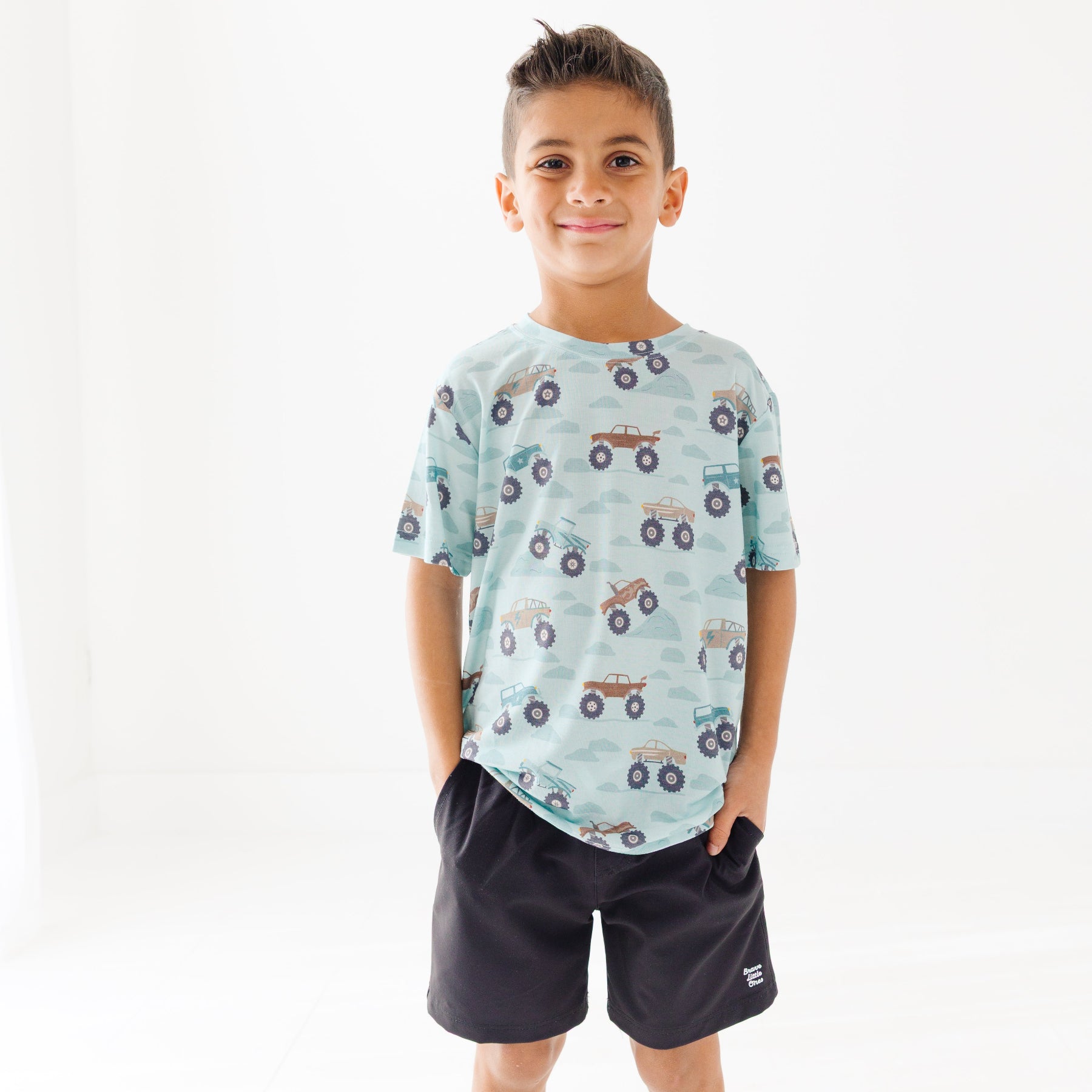 Child wearing a light blue t-shirt with vehicle patterns and black shorts on a white background