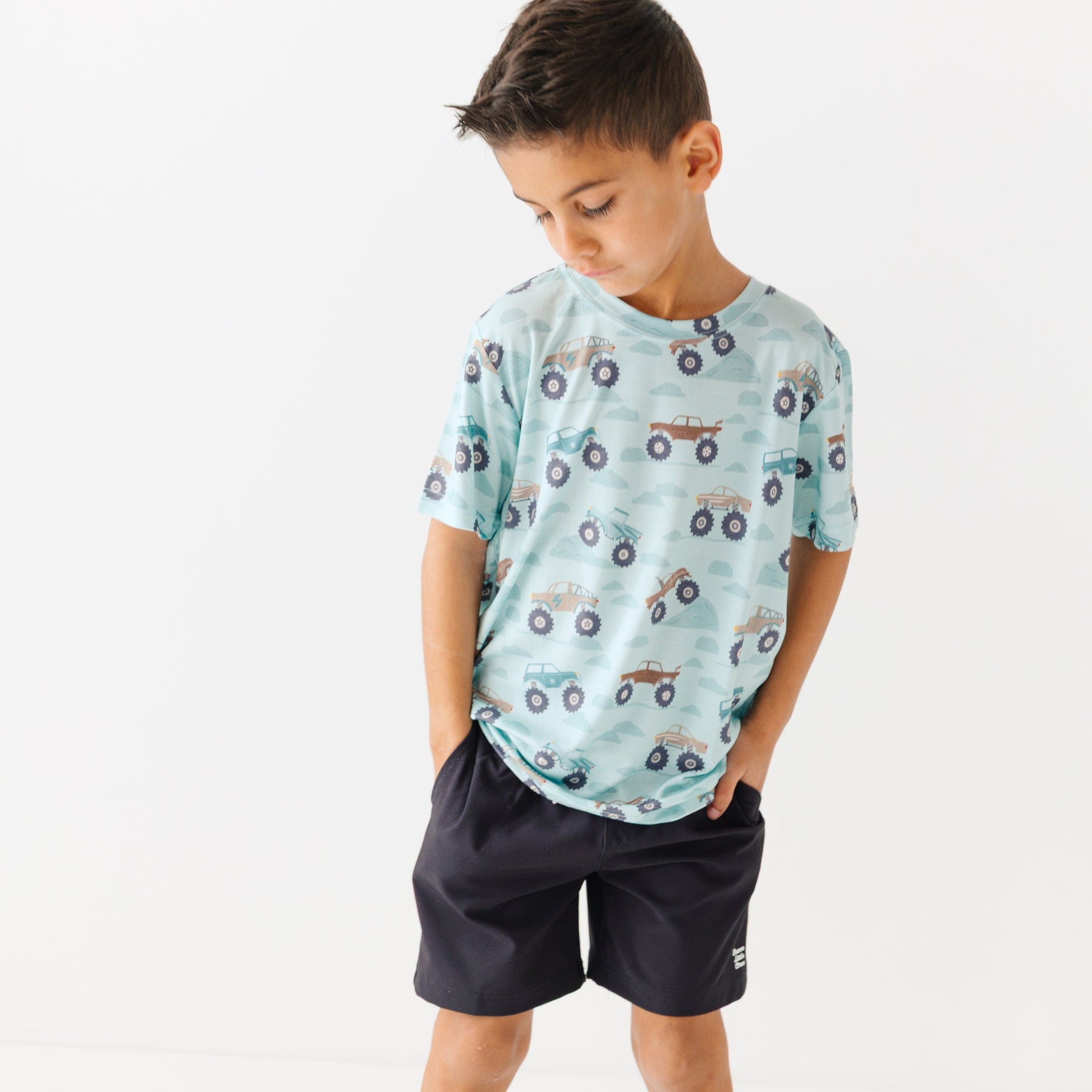 Child wearing a light blue t-shirt with vehicle pattern and black shorts on a white background