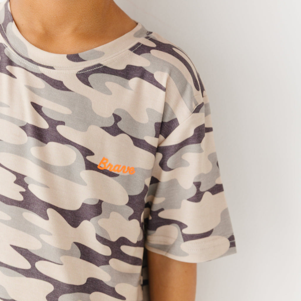 Close up shot of a child wearing a camouflage t-shirt with a brand logo on a plain background