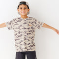 Child wearing a camouflage t-shirt, taupe cap and black shorts on a white background