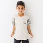 Child wearing a white t-shirt with checkered sleeves and black shorts on a white background