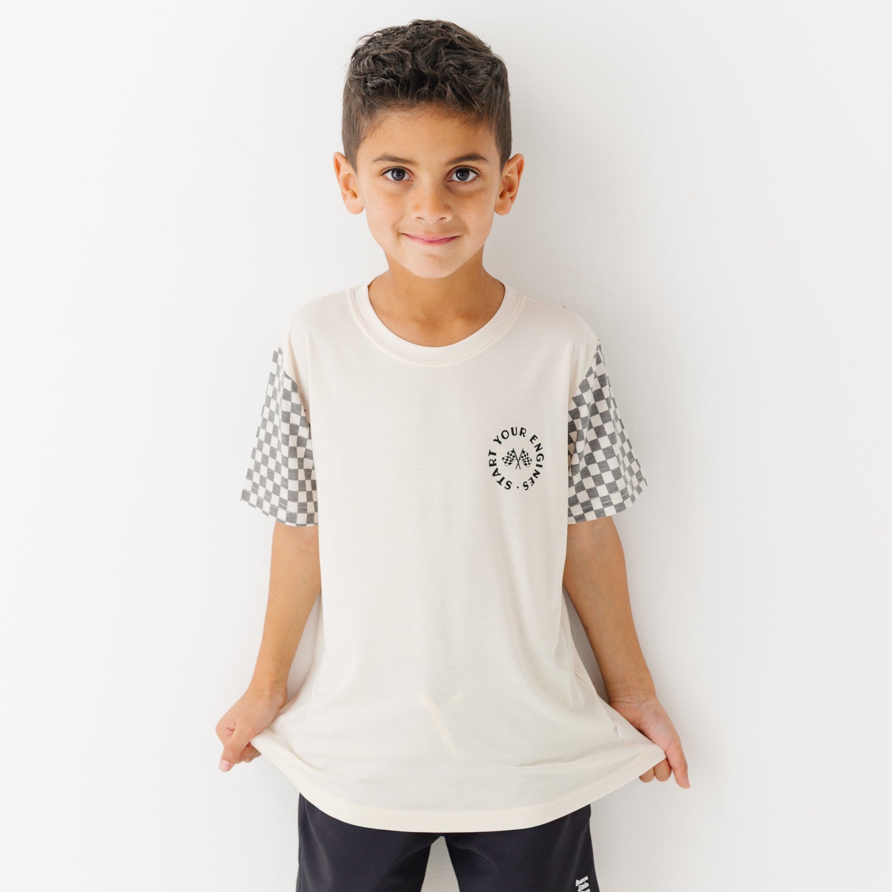Child wearing a white t-shirt with checkered sleeves and black shorts on a white background