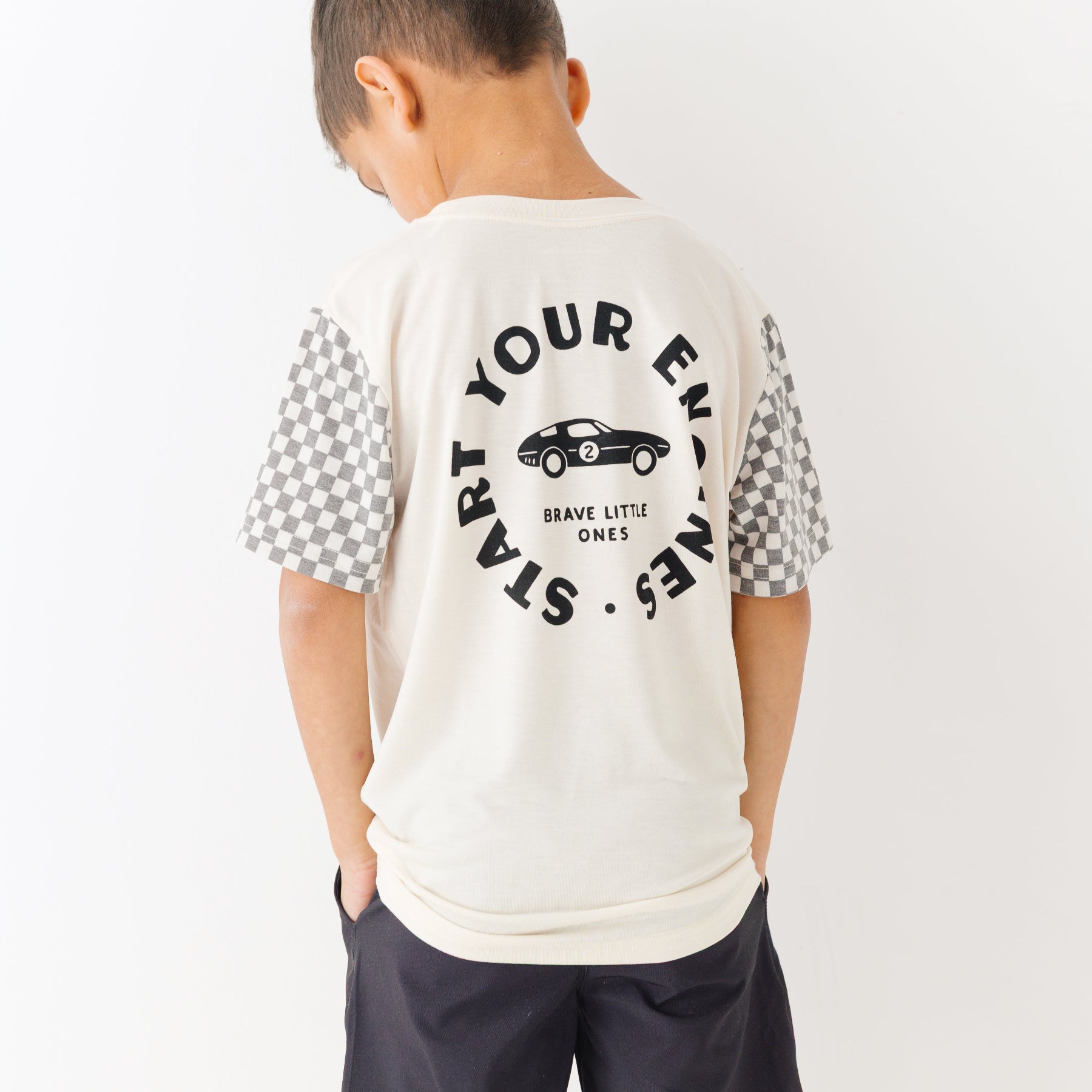 Child wearing a white t-shirt with text and checkered sleeves on a white background