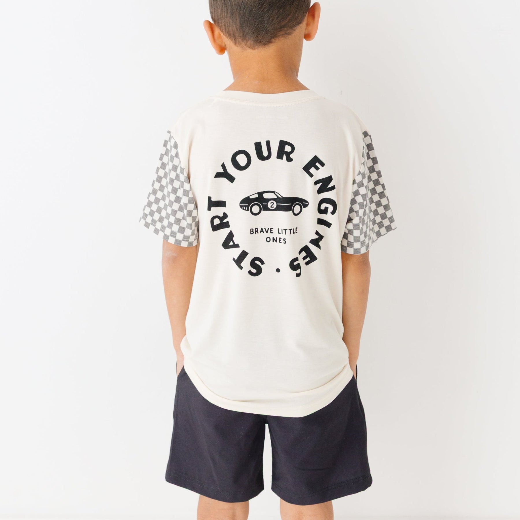 Child wearing a white t-shirt with logo and checkered sleeves and black shorts on a white background