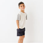 Child wearing a white t-shirt with checkered sleeves and black shorts on a white background
