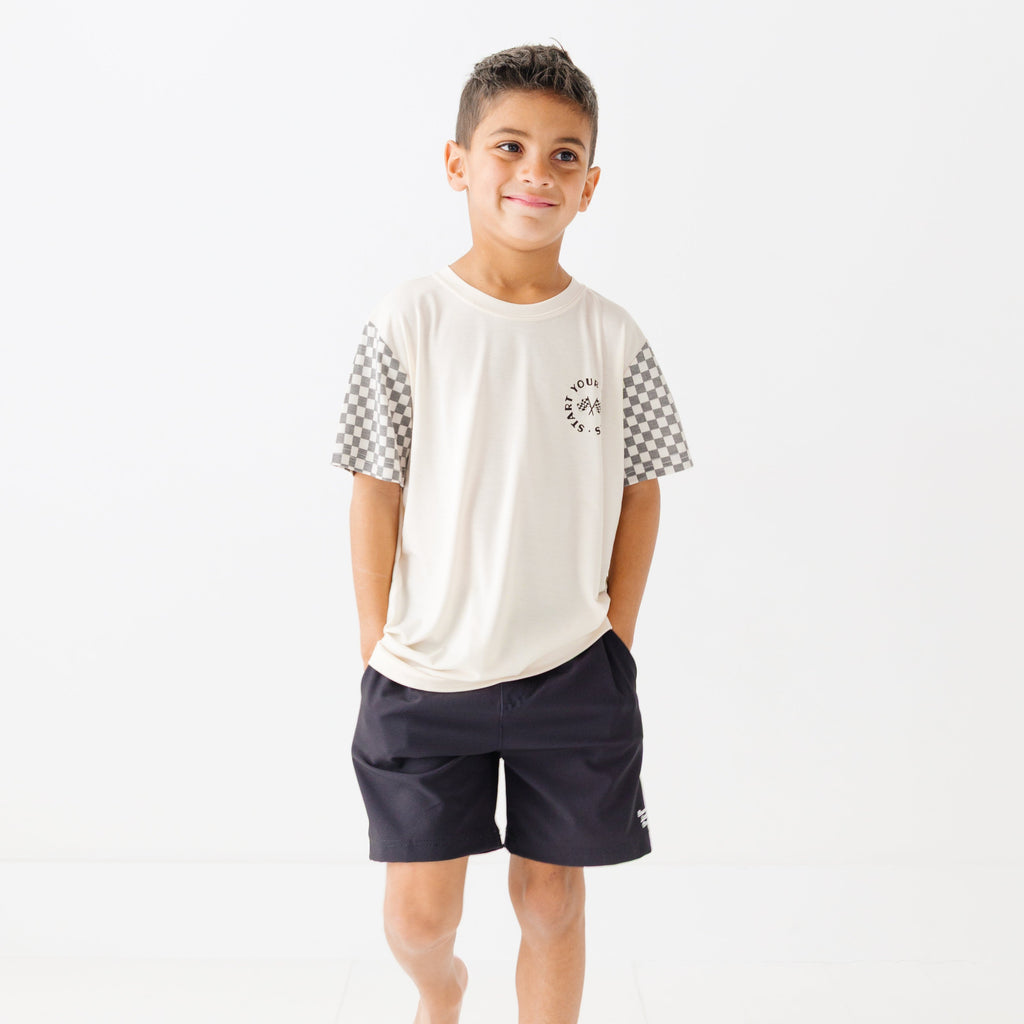 Child wearing a white t-shirt with checkered sleeves and black shorts on a white background